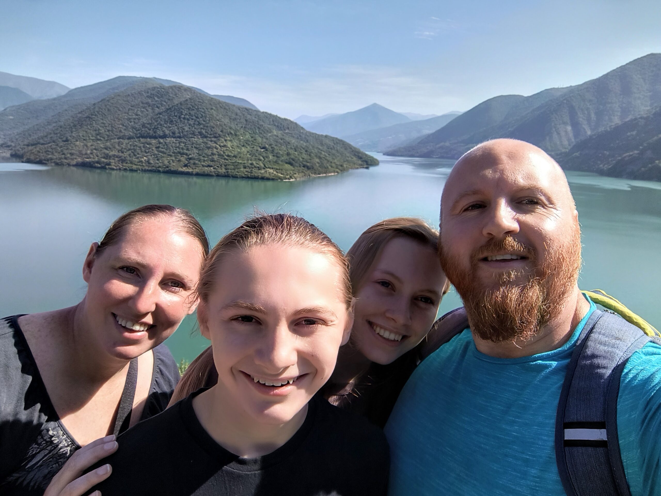 "Family of four smiling during a budget travel adventure at a scenic mountain lake viewpoint, showcasing the natural beauty of an affordable destination. Perfect moment captured on Life on a Bargain, a blog dedicated to budget-friendly family travel.